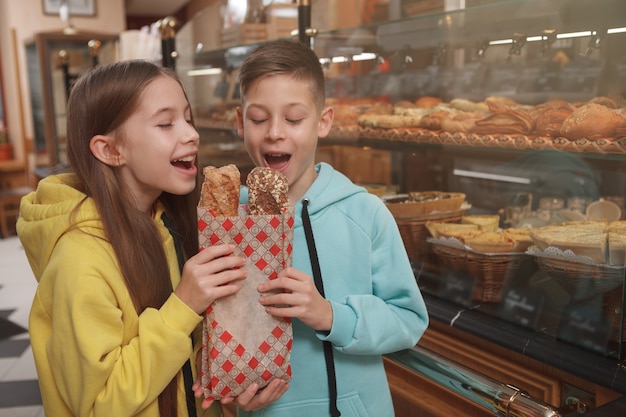 Vrolijke jonge tweelingen die heerlijk vers gebakken brood bijten bij bakkerijwinkel