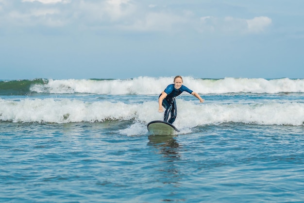 Vrolijke jonge vrouw beginner surfer met blauwe branding heeft plezier op kleine zeegolven. Actieve gezinslevensstijl, mensen buiten watersport les en zwemactiviteit op surfkamp zomervakantie.