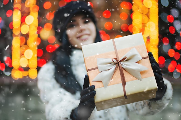 Vrolijke jonge vrouw die cadeau krijgt op de vakantiebeurs tijdens sneeuwval. Lege ruimte