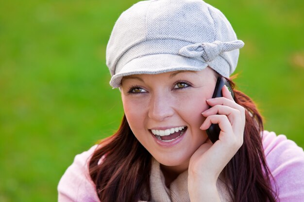 Vrolijke jonge vrouw die GLB en sjaal draagt ​​die op telefoon op het gras spreken