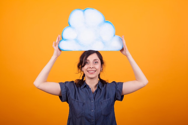 Vrolijke jonge vrouw die lacht naar de camera en een zware wolk op haar hoofd houdt in de studio op een gele achtergrond. kopieer beschikbare ruimte. meisje met lege gedachte plakkaat.