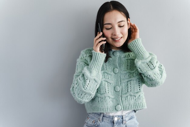 Vrolijke jonge vrouw die op mobiele telefoon spreekt die op grijze achtergrond wordt geïsoleerd