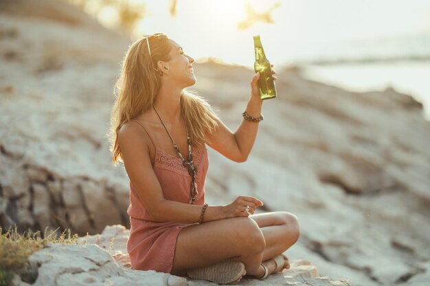 Vrolijke jonge vrouw die plezier heeft en bier drinkt op het strandfeest aan zee.