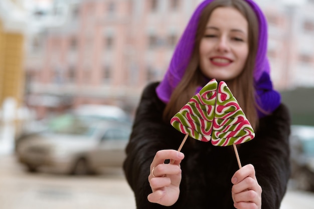 Vrolijke jonge vrouw die winteroutfit draagt, met smakelijke karamelsnoepjes. Vervagingseffect