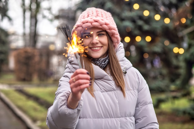 Vrolijke jonge vrouw draagt een roze gebreide muts en jas die plezier heeft met sterretjes op straat bij de kerstboom