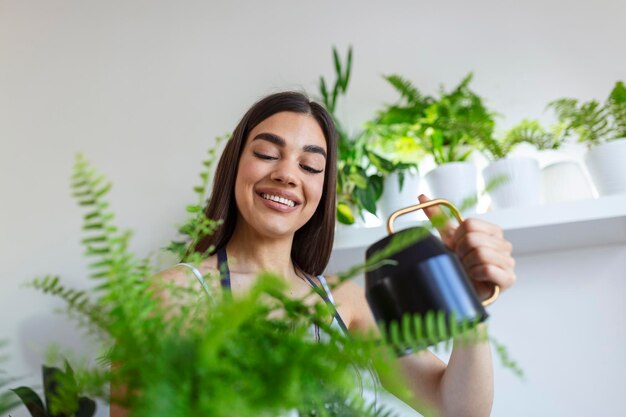 Vrolijke jonge vrouw geniet van haar tijd thuis en geeft haar plant water bij het raam thuis Vrouw zorgt voor haar varenwater aan de boom op een ontspannende dag in de tuin thuis