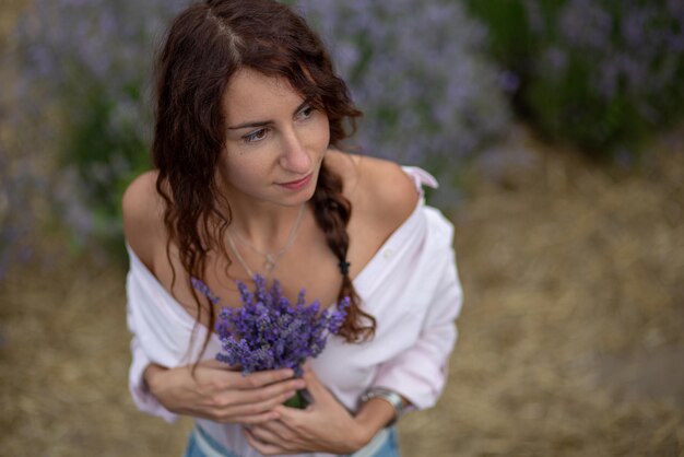 Vrolijke jonge vrouw genieten van lavendelveld met boeket bloemen