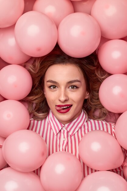 Vrolijke jonge vrouw in een hoop roze ballonnen tijdens feest