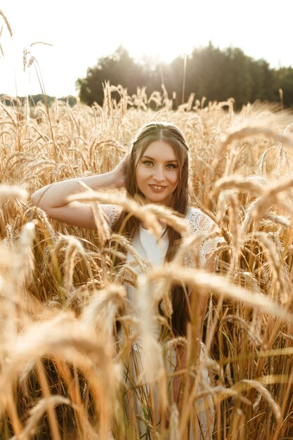 Vrolijke jonge vrouw in witte zomerjurk staande in tarweveld op zonnige dag