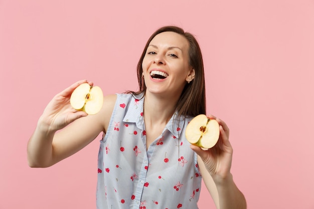 Vrolijke jonge vrouw in zomerkleren die helften van vers rijp appelfruit in handen houden geïsoleerd op roze pastelachtergrond in studio. mensen levendige levensstijl, ontspannen vakantie concept. bespotten kopie ruimte.