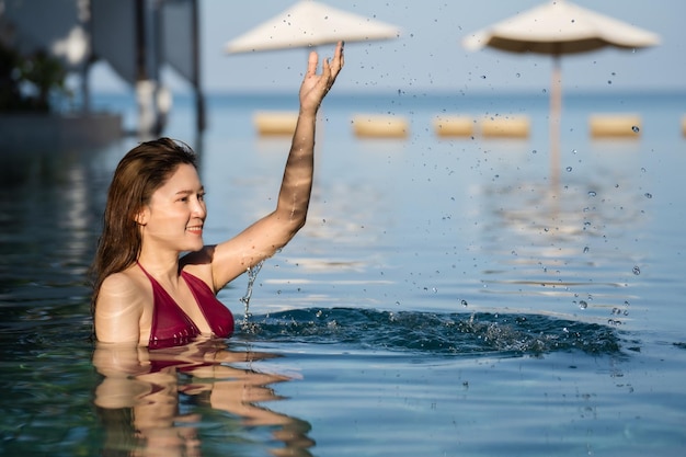 Vrolijke jonge vrouw in zwembroek spelen water spetteren in zwembad met zee achtergrond