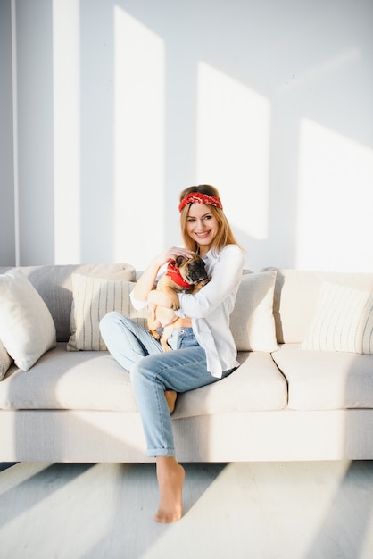 Vrolijke jonge vrouw met haar grote puppy met zwarte neus en lachen. Indoor portret van glimlachend meisje poseren met Franse bulldog