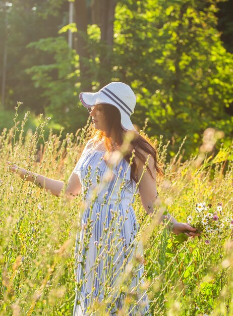 Vrolijke jonge vrouw met lang haar in hoed en jurk trekt haar handen naar de planten terwijl ze loopt