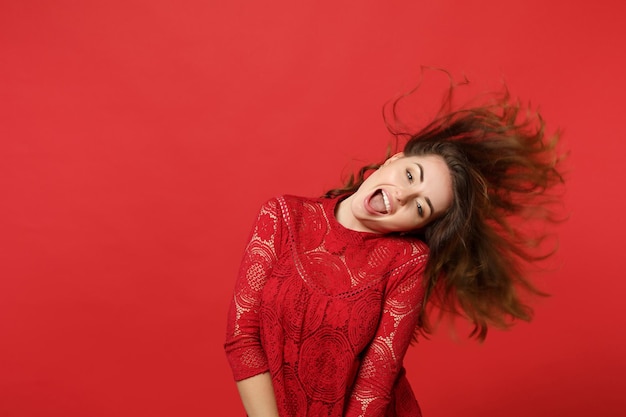 Vrolijke jonge vrouw met vliegend haar in kanten jurk die de mond openhoudt, gek rond geïsoleerd op een felrode muurachtergrond in de studio. Mensen oprechte emoties, lifestyle concept. Bespotten kopie ruimte.