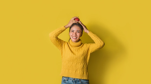 Vrolijke jonge vrouw op gele achtergrond in studio. Een lachend en gelukkig meisje met een appel op haar hoofd. Het concept van lichaamsbeweging voor een goede gezondheid. Gezondheidsliefhebber