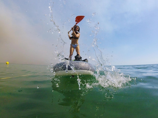 Foto vrolijke jonge vrouw staande op een opblaasbaar vlot in de zee tegen de lucht