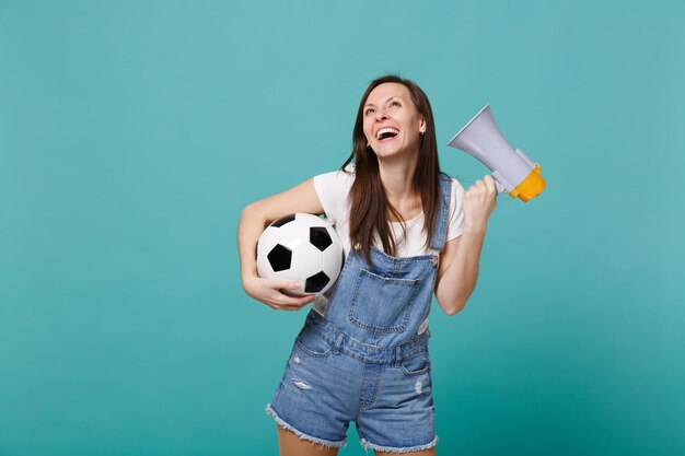 Vrolijke jonge vrouw voetbalfan ondersteuning favoriete team met voetbal, megafoon geïsoleerd op blauwe turkooizen achtergrond. mensen emoties, sport familie leisure lifestyle concept. bespotten kopie ruimte.