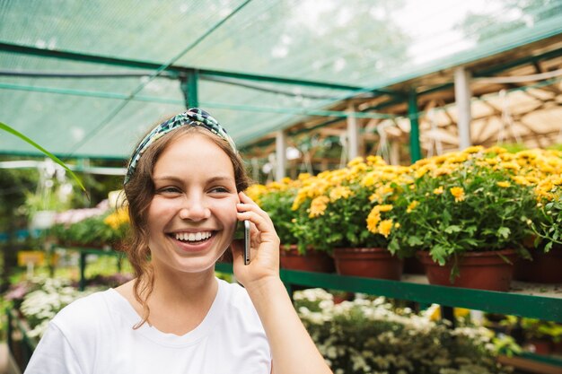 Vrolijke jonge vrouwelijke tuinman praten op mobiele telefoon