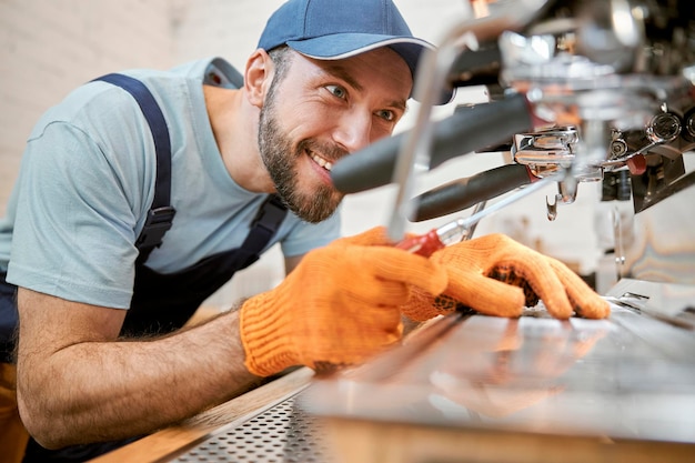 Vrolijke jongeman die koffiemachine in café repareert