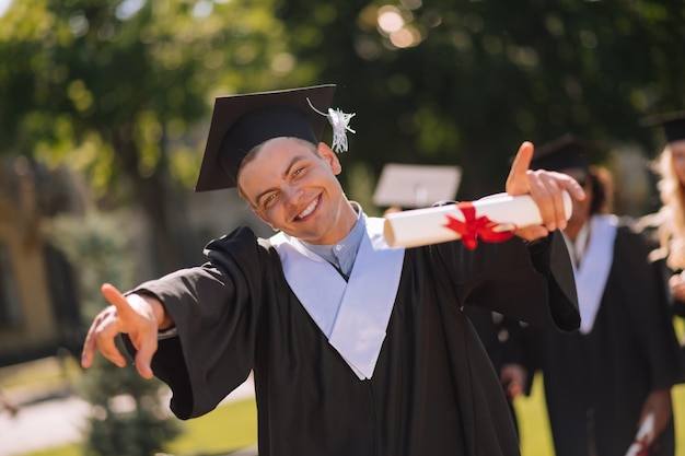 Vrolijke jongen die iedereen in de universiteitswerf zijn diploma toont