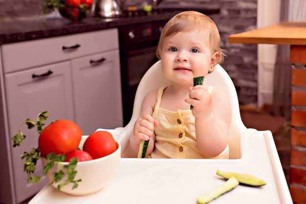 Vrolijke jongen groenten eten. Portret van een gelukkig meisje in een kinderstoel in de keuken