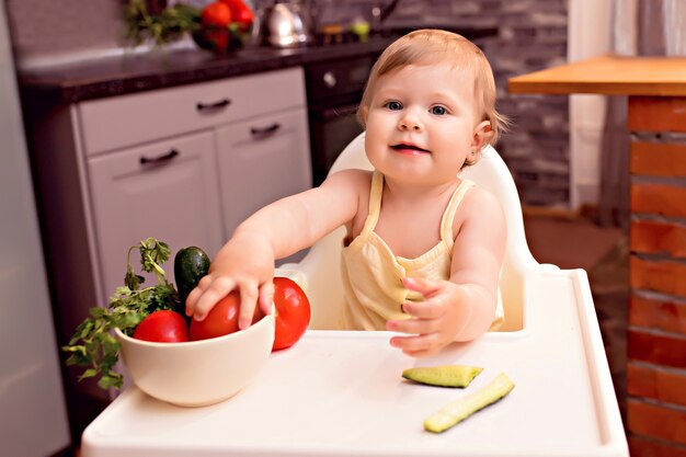 Vrolijke jongen groenten eten. Portret van een gelukkig meisje in een kinderstoel in de keuken