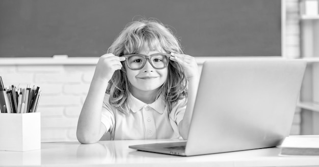 Vrolijke jongen met een bril studeert online in schoolklas met laptop september