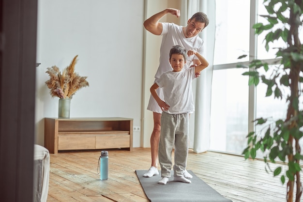 Vrolijke jongen met vader die biceps thuis laat zien