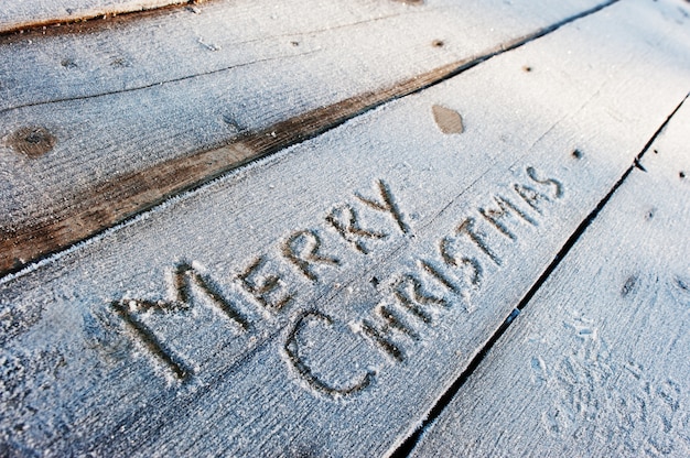 Vrolijke Kerstmis die op een houten vloer met vorst wordt geschreven