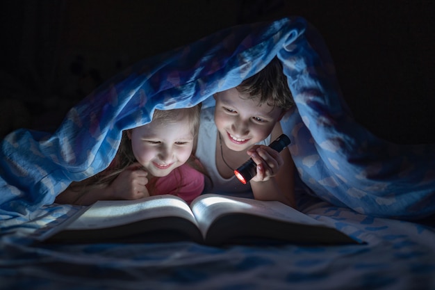 Vrolijke kinderen, broer en zus liggen onder de dekens en lezen een boek