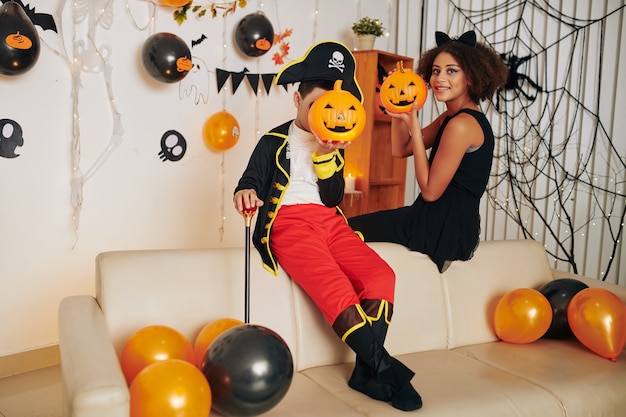 Vrolijke kinderen in Halloween-kostuums poseren met plastic jack-o-lanterns op huisfeest