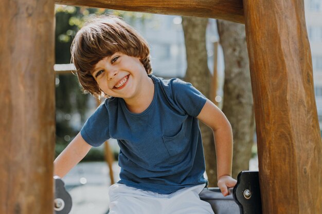 Vrolijke kleine jongen in een blauw T-shirt en witte korte broek speelt op een houten speelplaats. levensstijl. gezond actief kind loopt buiten. Hoge kwaliteit foto