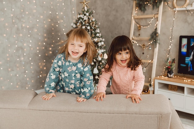 Vrolijke kleine kinderen, kleine meisjes springen op de bank lachend en plezier hebbend samen spelend thuis, kinderen genieten thuis van zorgeloze vrije tijd