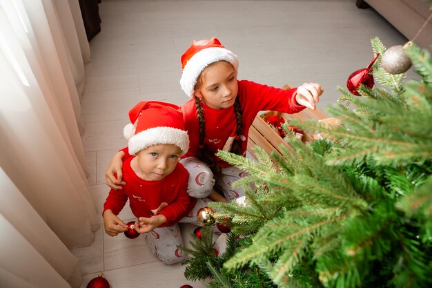 vrolijke knuffelende broer en zus in rode pyjama versieren de kerstboom in de woonkamer