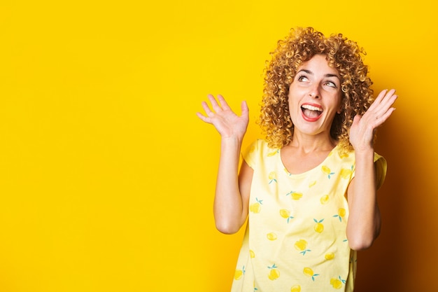 Vrolijke krullende jonge vrouw lachen handgebaren maken op gele achtergrond