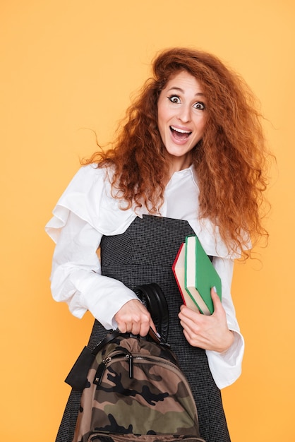 Vrolijke krullende jonge vrouw met rugzak en boeken