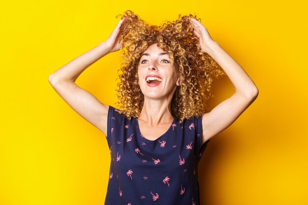 Foto vrolijke krullende jonge vrouw tilt haar haar op op een gele achtergrond.