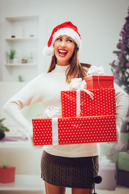 Vrolijke lachende vrouw met een kerstmuts op haar hoofd met cadeautjes.