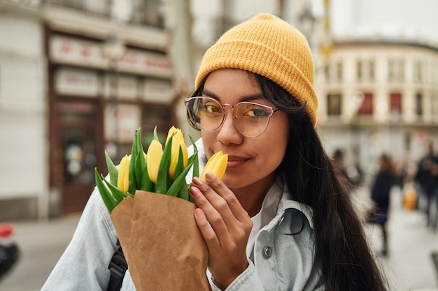 Vrolijke Latina die zonnige tulpen ruikt op levendige straat