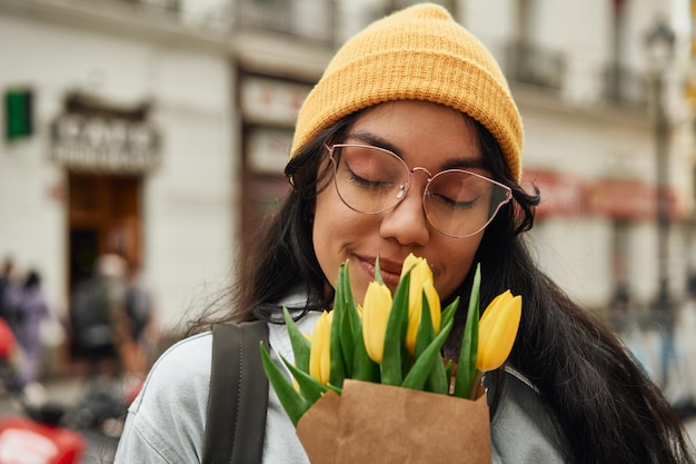 Vrolijke Latina die zonnige tulpen ruikt op levendige straat