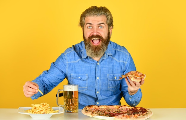 Vrolijke man bebaarde hipster eet pizza. Het concept van de pizzapartij. Geluk in de mond brengen. Bier en eten. Diner in kroeg. Hongerige man gaat pizza eten en bier drinken. Pizzeria-restaurant.