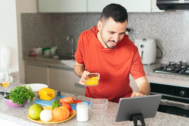 Vrolijke man die kookt en zijn tablet gebruikt in de keuken