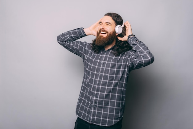 Vrolijke man die naar muziek luistert in een moderne koptelefoon en wegkijkt terwijl hij op een grijze achtergrond staat