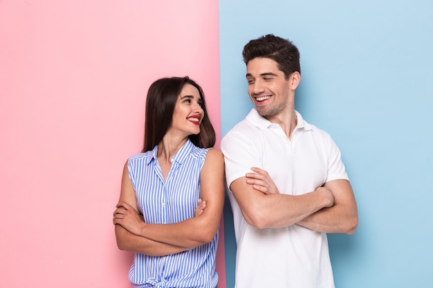 vrolijke man en vrouw in vrijetijdskleding staan met gekruiste armen, geïsoleerd over kleurrijke muur