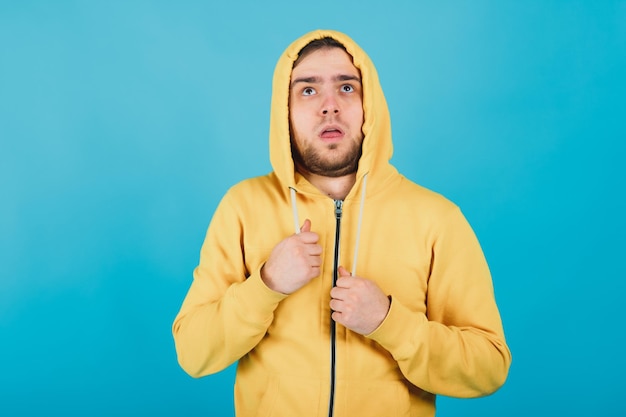 vrolijke man in een geel sweatshirt met capuchon kijkt in de camera en glimlacht tegen een blauwe achtergrond