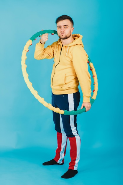 Vrolijke man in een gele blouse met een hoelahoep toont een voorkeur op een blauwe achtergrond