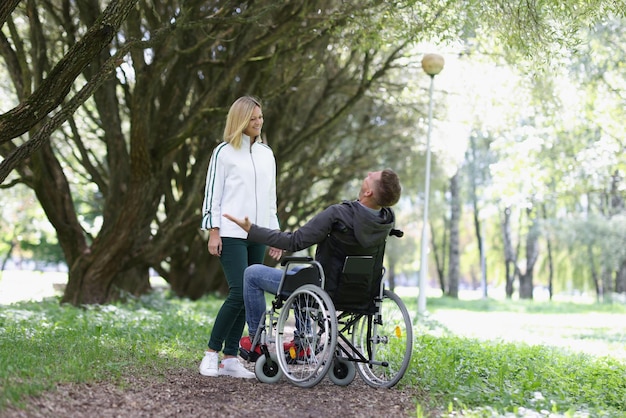 Vrolijke man in een rolstoel ontmoet vrouw in park en ontmoet vrienden in parkconcept