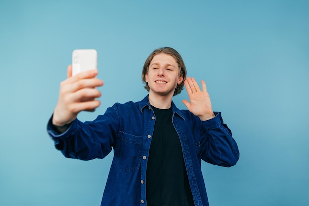 Vrolijke man in een shirt met een smartphone in zijn hand staat op een blauwe achtergrond