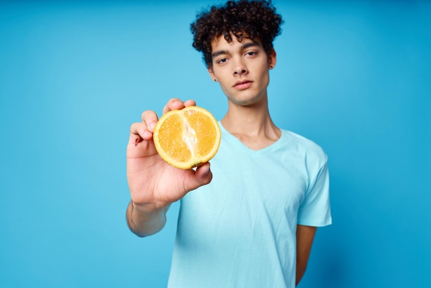 Vrolijke man met krullend haar met een oranje fruit blauwe achtergrond Foto van hoge kwaliteit