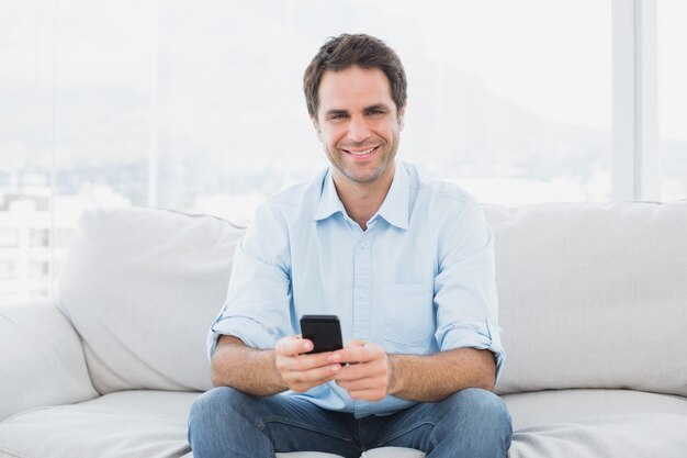 Vrolijke man zittend op de bank een SMS-bericht verzenden